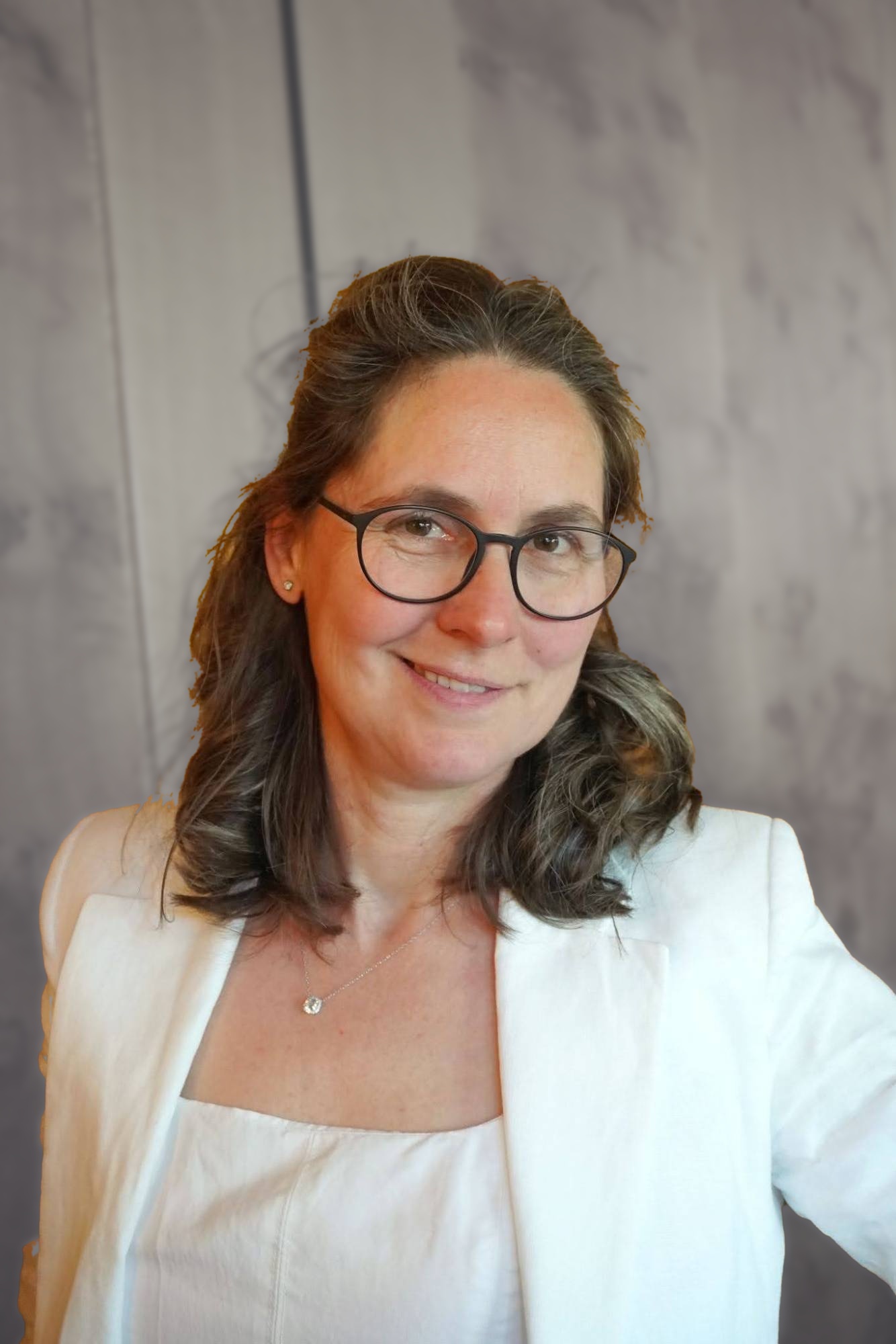 Sandra Donisi lächelt in die Kamera – braune, schulterlange Haare, dunkle Brille, weißer Blazer vor einem ruhigen, hellen Hintergrund.